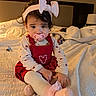 toddler, child, pacifier, headband, bow, red_dress, heart_design, bed, blanket, socks, indoors, portrait, cute, curly_hair, soft_lighting, cozy, person, baby, sitting, homedecor