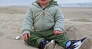 Jade joined the competition — help win amazing prizes! beach, blonde_hair, casual_clothing, child, cozy, cute, jacket, nature, ocean, outdoor, overcast_sky, pants, playful, portrait, sand, sitting, smile, sneakers, toddler, young_child