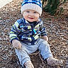 Jade is registered to the contest to win money with this photo: blue_eyes, casual_clothing, child, daylight, dirt, evergreen, face, happy, jacket, knit_hat, nature, outdoor, pants, person, playful, pom_pom, sitting, smiling, toddler, wood_chips