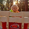baby, blonde_hair, cartoon_sticker, child, curly_hair, cute, forest, lightning_mcqueen, nature, outdoor, playful, red_wagon, smiling, sunlight, sunset, toddler, toy, trees, wagon, wooden_wagon