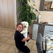Galak participe au concours pour gagner de l'argent avec cette photo : woman, person, dog, white_dog, pet, hugging, kneeling, smiling, portrait, indoors, living_room, home, houseplant, mirror, reflection, furniture, sideboard, chair, tiled_floor, wall_decor