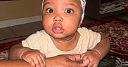 Tiana is registered to the contest to win money with this photo: baby, child, infant, hand, tattoo, headband, blanket, floor, indoor, person, skin, clothing, cute, expression, sitting, holding, pattern, furniture, carpet, adult