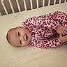 baby, infant, crib, mattress, pink_clothing, leopard_print, sleepwear, smiling, happy, child, cute, lying_down, indoors, face, head, hand, foot, earring, person, young
