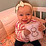Laÿna a rejoint le concours — aidez-le/la à gagner de superbes lots ! baby, smiling, headband, card, crib, pillow, blanket, striped_clothing, sitting, happy, infant, child, cute, indoors, flower_pattern, person, holding, face, cheerful, young