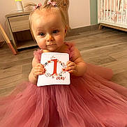 Laÿna a rejoint le concours — aidez-le/la à gagner de superbes lots ! baby, child, pink_dress, first_birthday, card, floor, giraffe_growth_chart, crib, hair_bows, tulle, cute, indoor, portrait, person, celebration, one_year_old, smiling, holding, sitting, young_child
