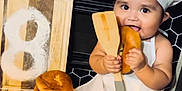 Aamiyah is registered to the contest to win money with this photo: baby, chef_hat, apron, kitchen, bread, bun, wooden_spatula, cutting_board, flour, countertop, smiling, cooking, child, sitting, foot, baking_tools, golden_spoons, black_tile, playful, cute