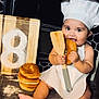 baby, chef_hat, apron, kitchen, bread, bun, wooden_spatula, cutting_board, flour, countertop, smiling, cooking, child, sitting, foot, baking_tools, golden_spoons, black_tile, playful, cute