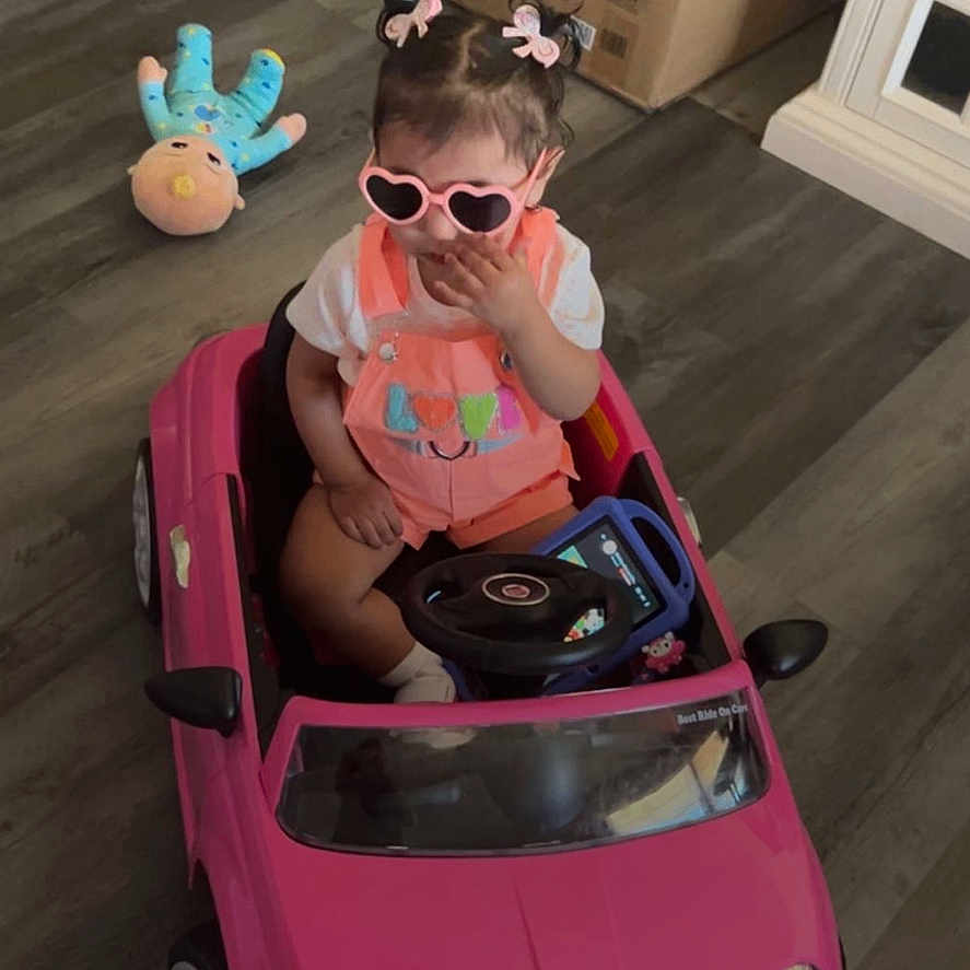 Zelda joined the competition — help win amazing prizes! toddler, child, toy_car, indoor, wooden_floor, stuffed_toy, pink, sunglasses, overalls, hair_bows, cardboard_box, floor, person, play, cute, seat, small_vehicle, baby, home, notification