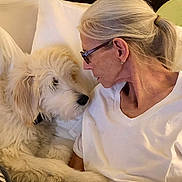 Clarabelle joined the competition — help win amazing prizes! affection, bed, blanket, blonde_hair, closeup, cozy, cuddling, dog, face, fluffy_fur, glasses, indoors, person, pet, pillows, ponytail, portrait, warm_lighting, white_shirt, woman