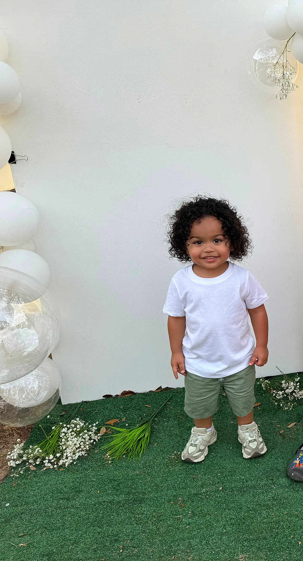 Azhainei joined the competition — help win amazing prizes! background, balloons, casual_clothing, celebration, child, curly_hair, cute, flowers, green_grass, green_shorts, happy, nature, outdoor, person, portrait, smiling, sneakers, standing, toddler, white_tshirt