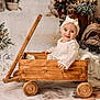 baby, child, wagon, wooden_wagon, white_dress, bow_headband, winter_decor, pine_cones, christmas_tree, holiday_theme, smiling, portrait, indoor, cozy, decorations, cute, infant, festive, soft_lighting, warm_colors