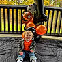 Liam is registered to the contest to win money with this photo: toddler, child, baby, smiling, orange_shirt, camo_jacket, jeans, white_socks, balloons, halloween, ghost_balloon, pumpkin_balloon, number_one_balloon, black_blanket, outdoor, autumn, fall_leaves, porch, wooden_railing, happy