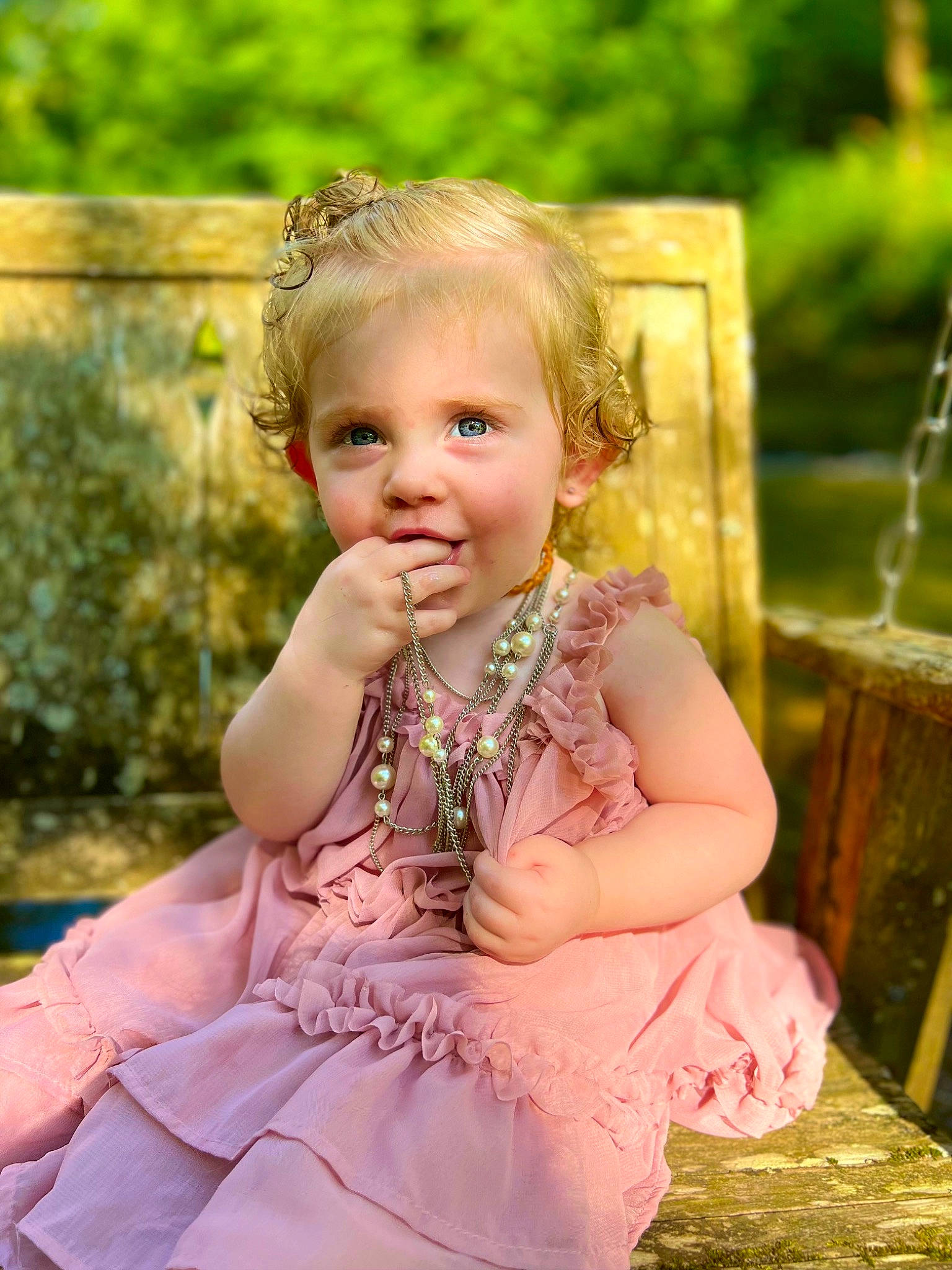 Ila is registered to the contest to win money with this photo: baby, baby_toddler_clothing, blond, child, dress, fun, grass, green, hairstyle, happy, iris, leisure, pattern, peach, people_in_nature, person, pink, plant, sitting, smile