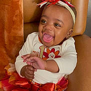 Kaniyah is registered to the contest to win money with this photo: baby, child, smiling, laughing, headband, bow, striped_leggings, tutu_skirt, orange, white, red, chair, indoor, happy, cute, infant, person, portrait, celebration, clothing