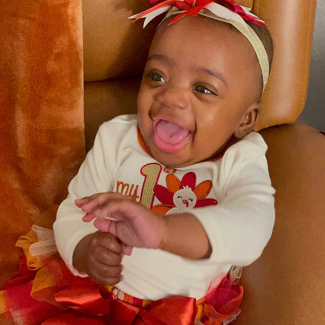 Kaniyah is registered to the contest to win money with this photo: baby, child, smiling, laughing, headband, bow, striped_leggings, tutu_skirt, orange, white, red, chair, indoor, happy, cute, infant, person, portrait, celebration, clothing