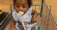 Sarai joined the competition — help win amazing prizes! aisle, baby, bows, child, curly_hair, cute, floor, grocery_store, hand, holding, indoor, infant, metal_bar, pacifier, person, produce, seat, shopping_cart, sitting, striped_dress