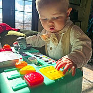 Elend is registered to the contest to win money with this photo: baby, child, toy, keyboard, microphone, light, sunlight, window, indoor, furniture, bow_tie, clothing, playing, colorful, hand, face, curious, table, person, room