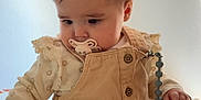 Amalya a rejoint le concours — aidez-le/la à gagner de superbes lots ! baby, pacifier, beige_clothing, sitting, blanket, pattern, curious, indoor, child, infant, cute, young, portrait, soft_lighting, hands, face, head, long_sleeves, buttons, ruffles