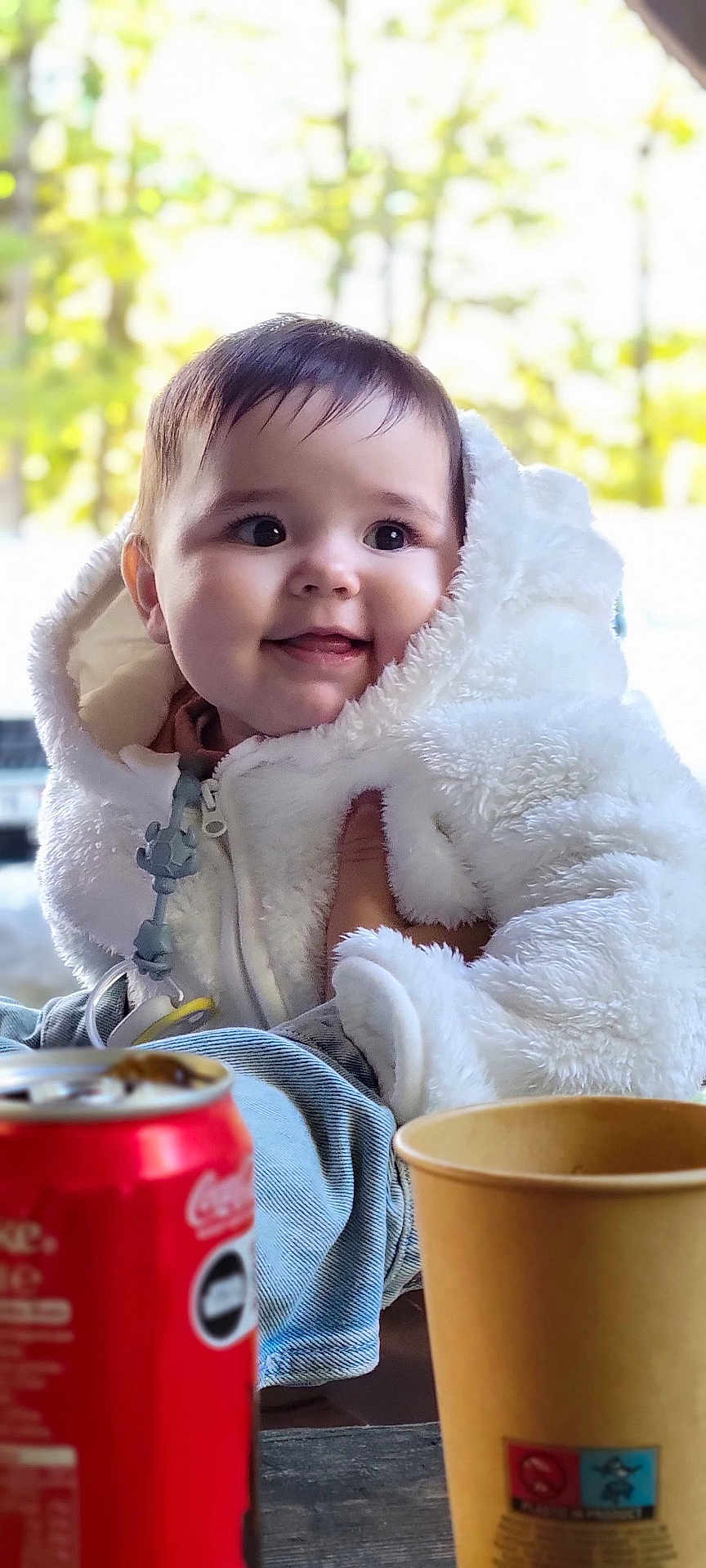 Amalya a rejoint le concours — aidez-le/la à gagner de superbes lots ! baby, child, smiling, face, white_jacket, fluffy_clothing, hand, indoor, cup, soda_can, foreground, soft_light, portrait, cute, young, person, jeans, table, warm_clothing, cozy