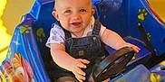 Maëlyo a rejoint le concours — aidez-le/la à gagner de superbes lots ! baby, child, amusement_ride, kiddie_ride, steering_wheel, blue_car, cartoon_characters, outdoor, daylight, smiling, happy, playful, shorts, overalls, seat, toy_car, bright_colors, sunlight, face, eyes