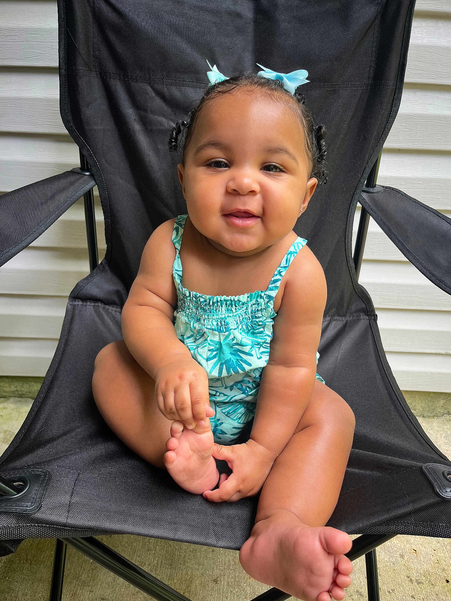 Ava joined the competition — help win amazing prizes! baby, child, smiling, sitting, blue_bows, black_chair, outdoor, concrete, summer_clothing, cute, happy, person, infant, skin, foot, hand, playful, portrait, green_pattern, hair
