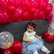 Amber joined the competition — help win amazing prizes! toddler, girl, balloons, red_balloons, transparent_balloons, dress, blue_dress, white_tights, red_boots, headband, red_bow, couch, gray_couch, indoor, celebration, party, child, sitting, curious, festive