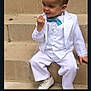 accessory, bow_tie, boy, casual_pose, child, cute, footwear, formal_wear, outdoor, person, playful, portrait, short_hair, sitting, smiling, stairs, stone_steps, toddler, white_shoes, white_suit
