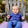baby, child, smiling, blue_clothing, striped_shirt, pants, barefoot, wooden_chair, cushion, outdoor, nature, greenery, sunlight, portrait, happy, sitting, face, person, cute, young