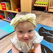 Aurelia joined the competition — help win amazing prizes! baby, blue_eyes, child, colorful, crawling, cute, furniture, happy, headband, indoor, infant, person, play_mat, portrait, shelf, smiling, toys, wooden_floor, yellow_bow, young_child