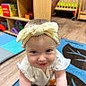 baby, blue_eyes, child, colorful, crawling, cute, furniture, happy, headband, indoor, infant, person, play_mat, portrait, shelf, smiling, toys, wooden_floor, yellow_bow, young_child