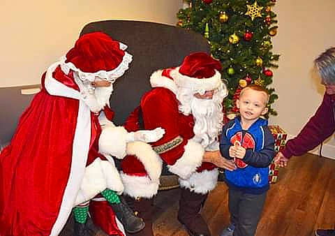 August is registered to the contest to win money with this photo: christmas, christmas_decoration, christmas_eve, christmas_ornament, christmas_tree, costume_hat, event, fictional_character, fur, fur_clothing, hat, holiday, lap, outerwear, person, santa_claus, smile, toddler, tradition, tree