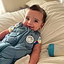 baby, smiling, blue_outfit, bed, pillow, baby_bottle, infant, cute, child, lying_down, soft_toys, comfortable, indoors, cozy, sleepwear, portrait, young_child, happy, baby_clothing, resting