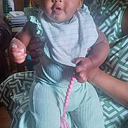Kennedi is registered to the contest to win money with this photo: adult_hand, baby, bib, child, curtains, flower, furniture, happy, headband, indoors, infant, lamp, living_room, mint_outfit, person, pink_beads, portrait, smiling, toy, wood_paneling