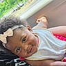 Kennedi is registered to the contest to win money with this photo: baby, child, headband, smile, curly_hair, bib, car_interior, seat, natural_light, outdoor, greenery, window, pink_clothing, cute, infant, relaxed, portrait, skin, happy, person