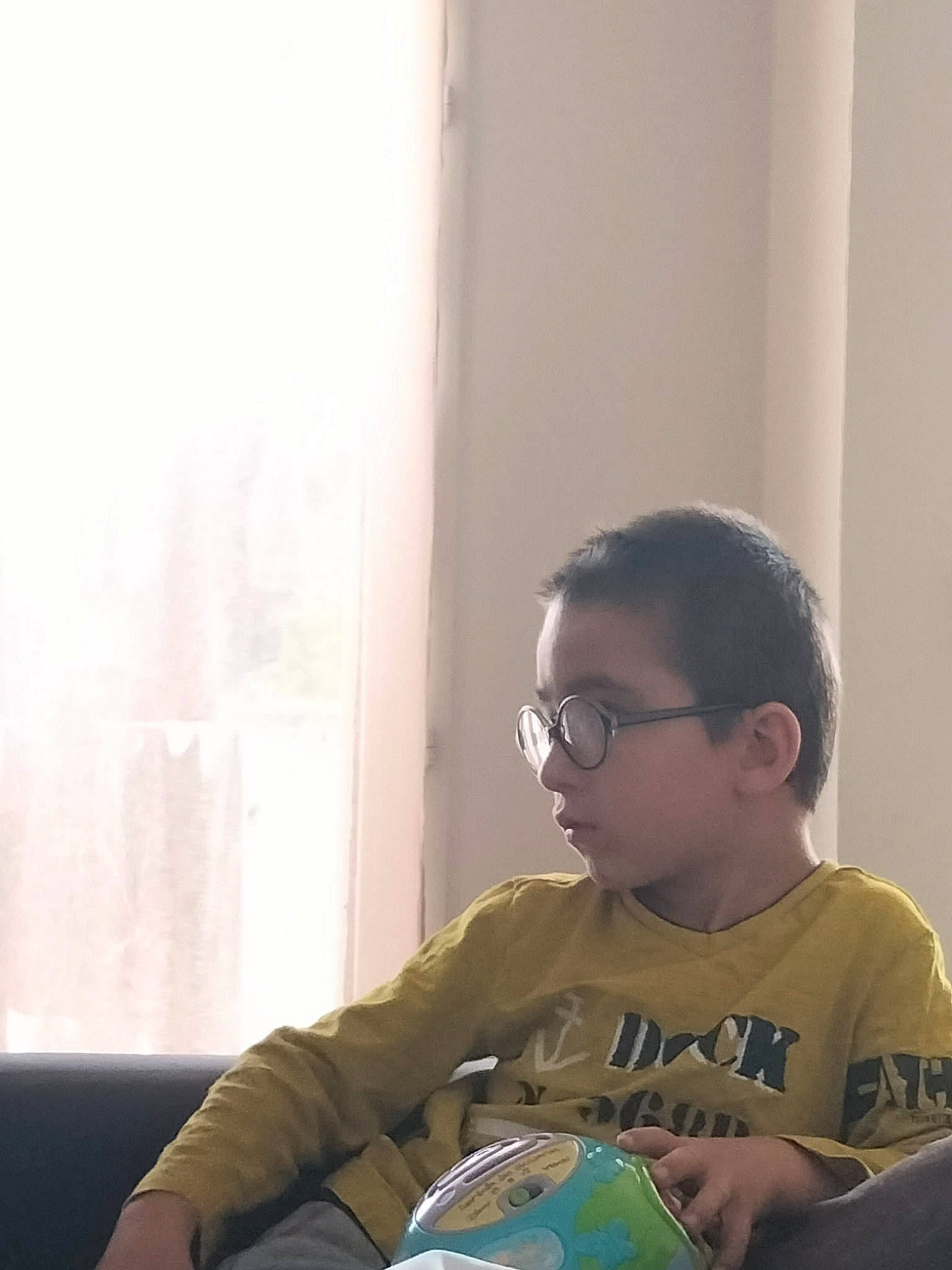 Julian participe au concours pour gagner de l'argent avec cette photo : child, comfort, eyewear, football, fun, glass, glasses, happy, person, reading, room, sitting, t_shirt, toddler, toy, vision_care, window