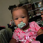 Talitha joined the competition — help win amazing prizes! baby, blanket, bottle, child, curly_hair, cute, expression, face, furniture, hand, home, indoor, pacifier, person, pink_clothing, sitting, storage_boxes, table, toddler, toy