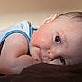 baby, infant, close_up, face, skin, arm, eyes, laying_down, resting, white_shirt, blue_trim, soft_light, indoors, portrait, cute, child, young, expression, skin_texture, warm_background