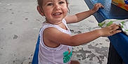 Harmony is registered to the contest to win money with this photo: blue_bench, box, casual_clothing, child, concrete_floor, daylight, drink_can, fanta, hair_bun, hand, happy, open_mouth, outdoor, person, picnic_table, playful, sitting, smiling, toddler, white_tank_top