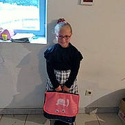 Kimberley participe au concours pour gagner de l'argent avec cette photo : black_top, cat_illustration, checkered_skirt, child, floor_tiles, footwear, girl, glasses, hair_tie, home_interior, indoor, light, person, picture_frame, school_bag, shadow, smile, standing, wall, window