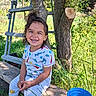 child, smile, outdoor, tree, grass, bucket, bench, ladder, sunlight, nature, happy, clothing, patterned_shirt, pants, footwear, hair, wood, greenery, playful, daylight