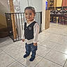 baby_gate, boy, cabinet, child, curtains, cute, dining_chairs, furniture, happy, home_interior, indoor, jeans, person, portrait, smile, socks, standing, tile_floor, vest, wooden_furniture