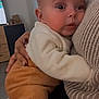 baby, infant, child, holding, cuddle, hand, sweater, knit, pants, onesie, close_up, portrait, indoor, living_room, furniture, gaze, big_eyes, skin, cozy, caregiver_hand