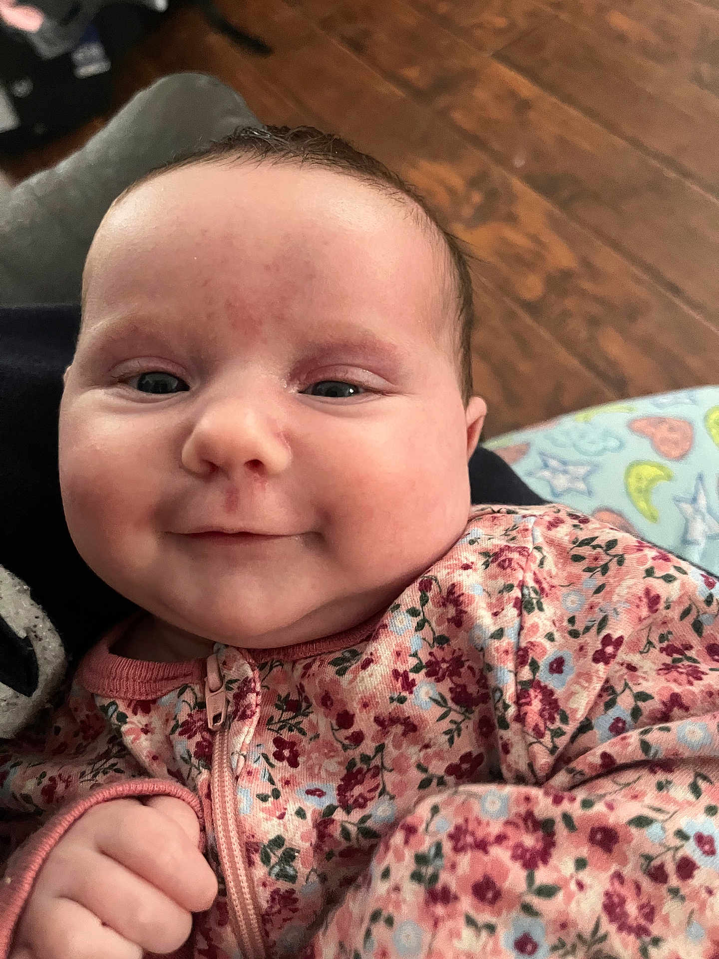 Marleigh is registered to the contest to win money with this photo: baby, infant, smile, cheeks, face, portrait, floral_pajamas, hand, fist, close_up, wooden_floor, blanket, pattern, indoor, cute, eyes, skin, head, clothing, happy