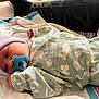 baby, newborn, sleeping, pacifier, beanie, hospital_blanket, onesie, mint_color, floral_pattern, swaddled, tiny_hand, hospital_bed, camo_pants, adult_leg, towel, portrait, closeup, peaceful, soft_texture, infant_clothing