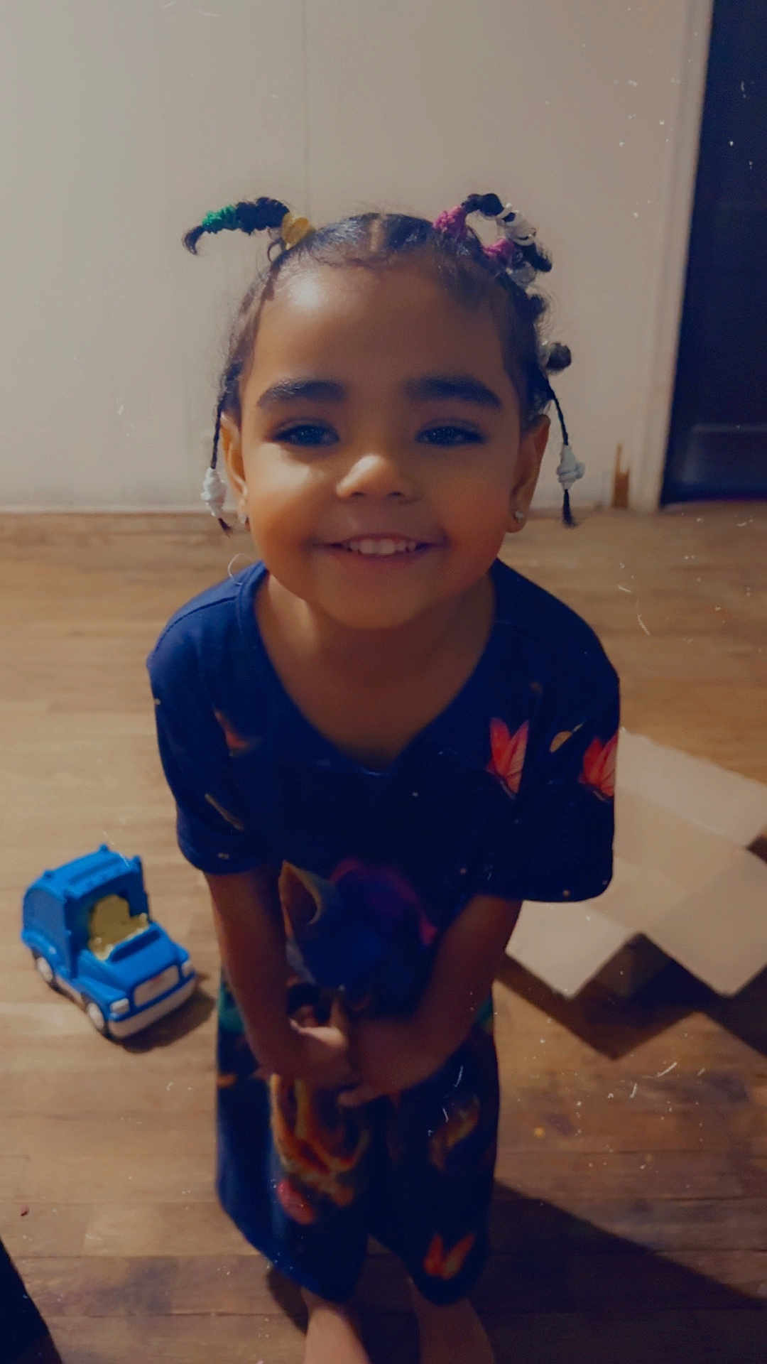 Alia is registered to the contest to win money with this photo: child, smile, braided_hair, toy_truck, cardboard_box, wooden_floor, happy, indoor, person, footwearless, colorful_clothing, girl, playtime, cute, standing, childhood, joyful, home, portrait, casual