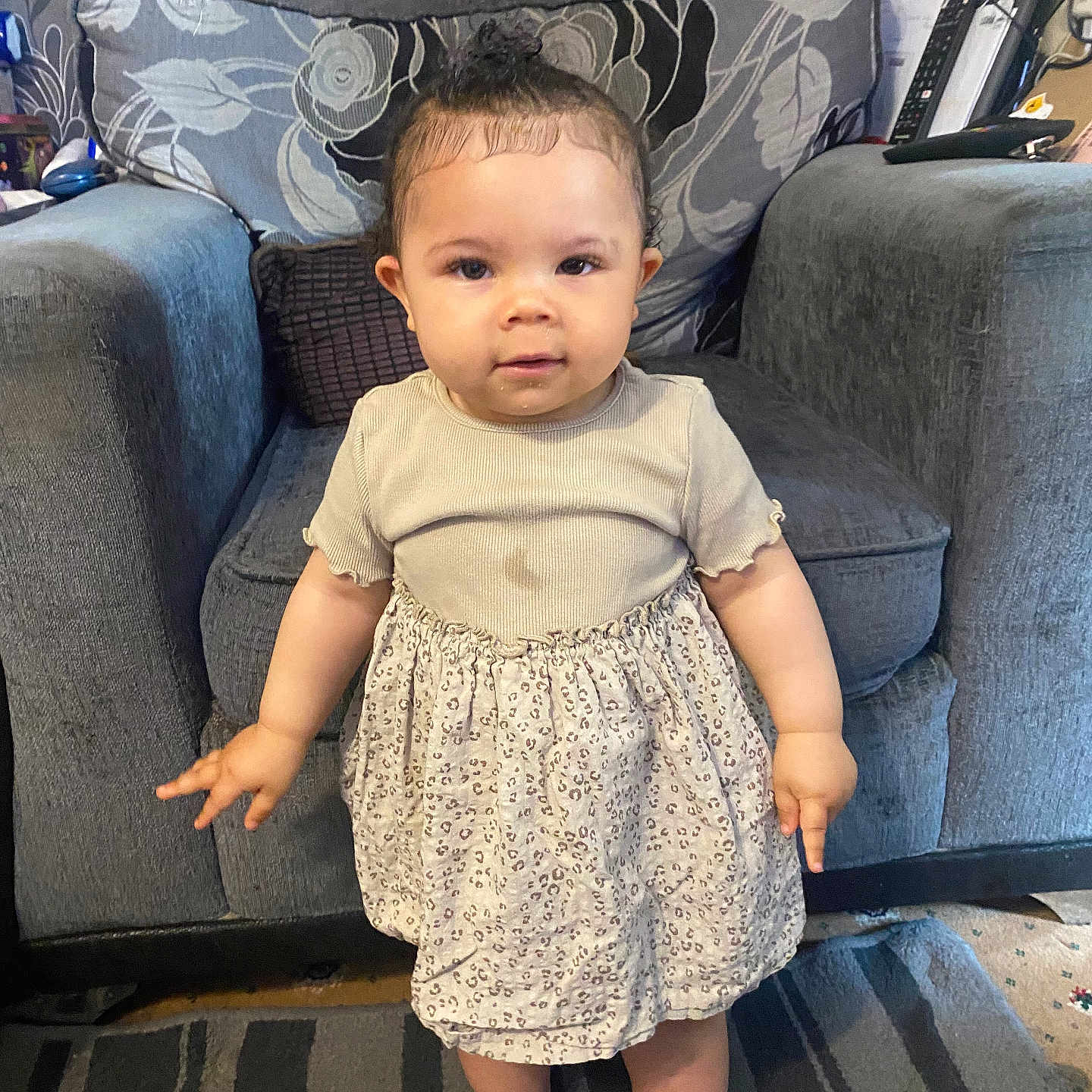 Harmony-Mai joined the competition — help win amazing prizes! baby, barefoot, beige_top, carpet, child, clothing, couch, curious_expression, furniture, gray_couch, home, indoor, living_room, patterned_skirt, person, sofa, standing, striped, toddler, young_child