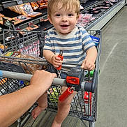 Noah is registered to the contest to win money with this photo: toddler, child, shopping_cart, grocery_store, striped_shirt, smiling, barefoot, shopping, food, aisle, bread, packaged_meat, floor, hand, person, supermarket, happy, baby, retail, store