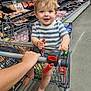 toddler, child, shopping_cart, grocery_store, striped_shirt, smiling, barefoot, shopping, food, aisle, bread, packaged_meat, floor, hand, person, supermarket, happy, baby, retail, store
