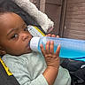 baby, child, infant, car_seat, bottle, water, drinking, portrait, face, hand, eyes, smiling, indoors, vehicle, safety_harness, gray_clothing, blue_bottle, close_up, seated, transportation