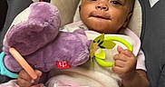 Damarionna is registered to the contest to win money with this photo: baby, child, car_seat, plush_toy, purple_toy, blanket, infant, smiling, holding, cute, indoors, soft_toy, person, seat, comfort, young_child, striped_blanket, hand, face, portrait